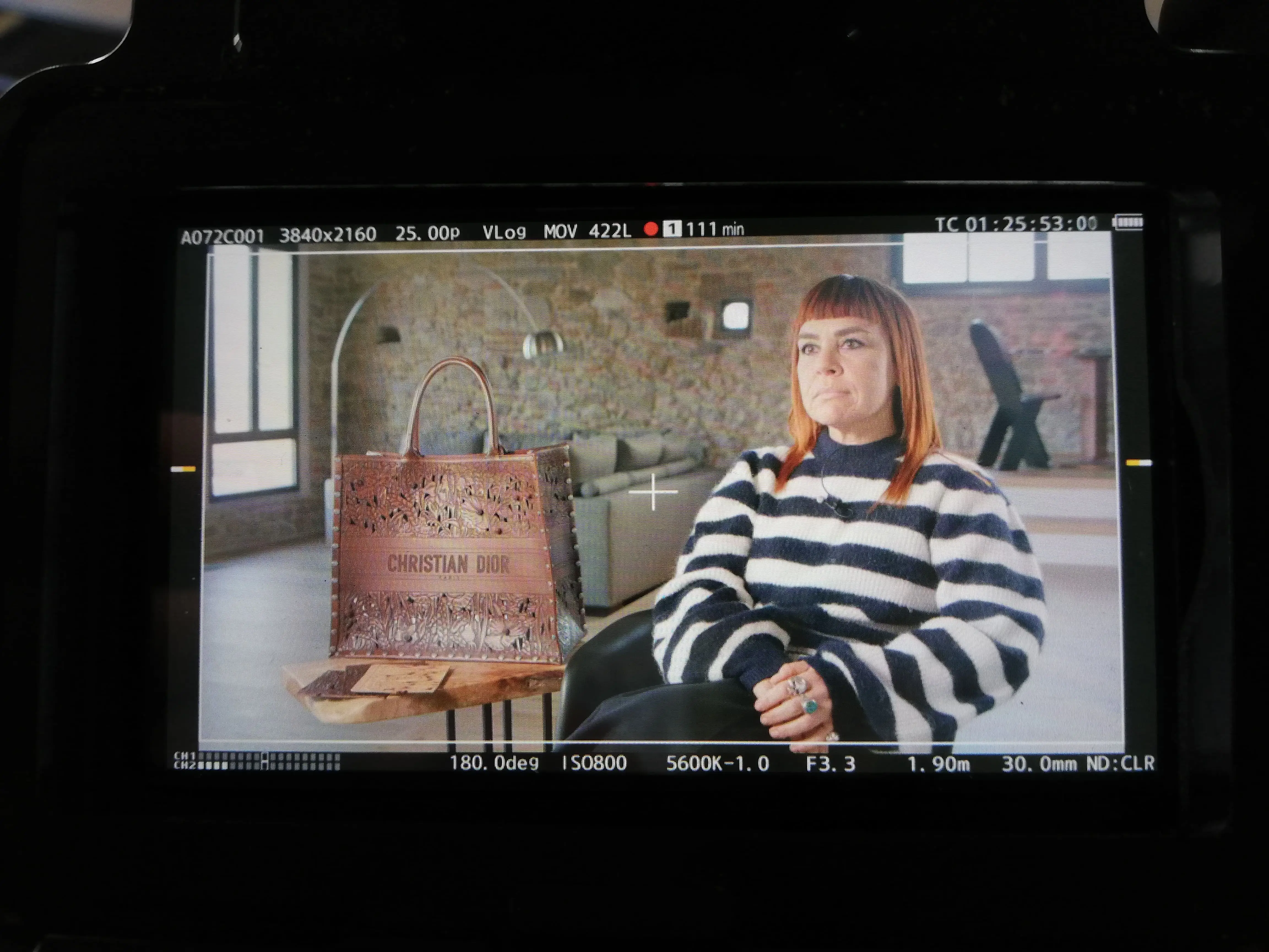 Field monitor showing a framed interview on a Dior shoot, with a handbag in shot beside the subject