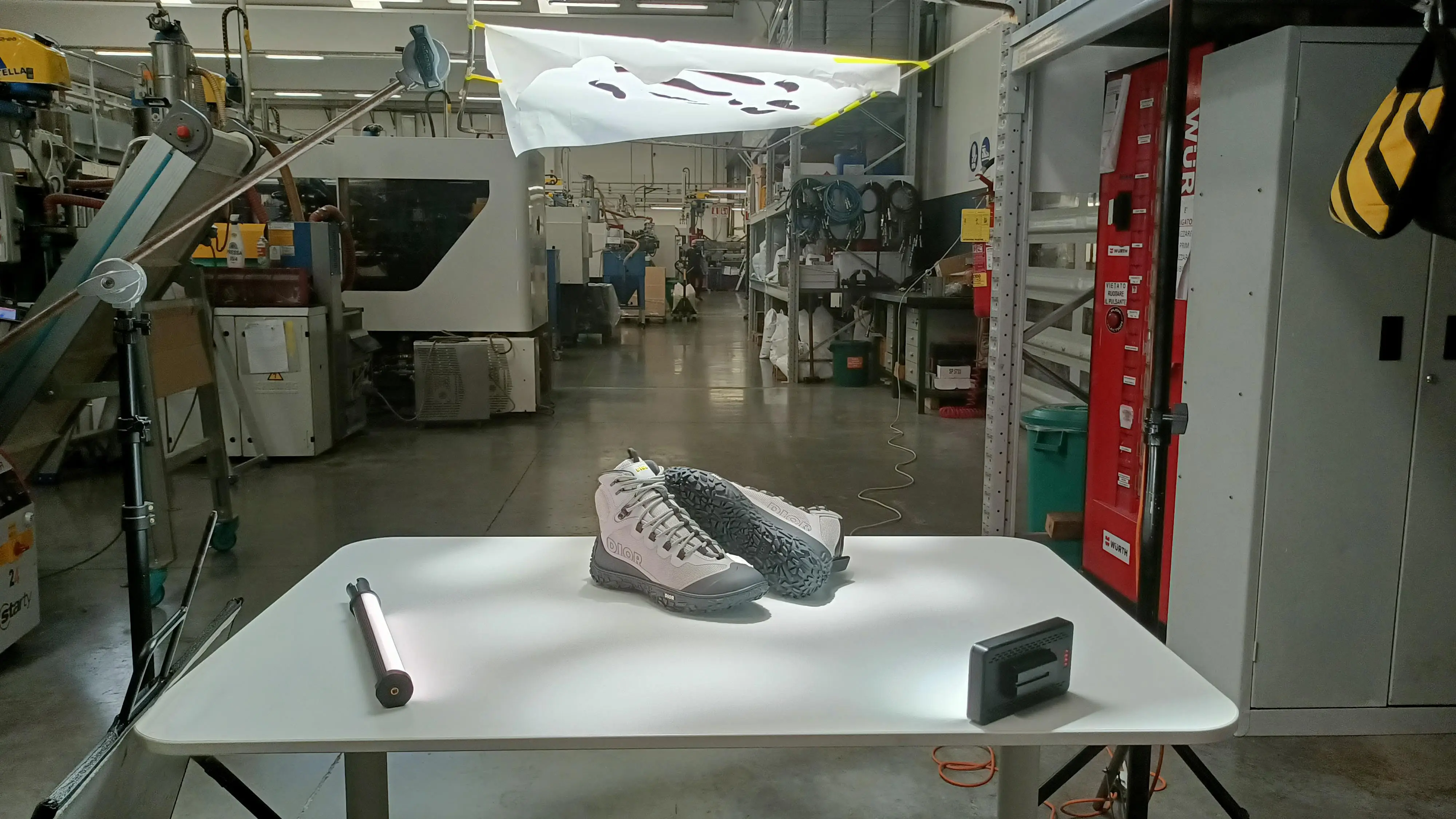 Small white table set up with a Dior sneaker and a lighting rig in the middle of a working factory floor