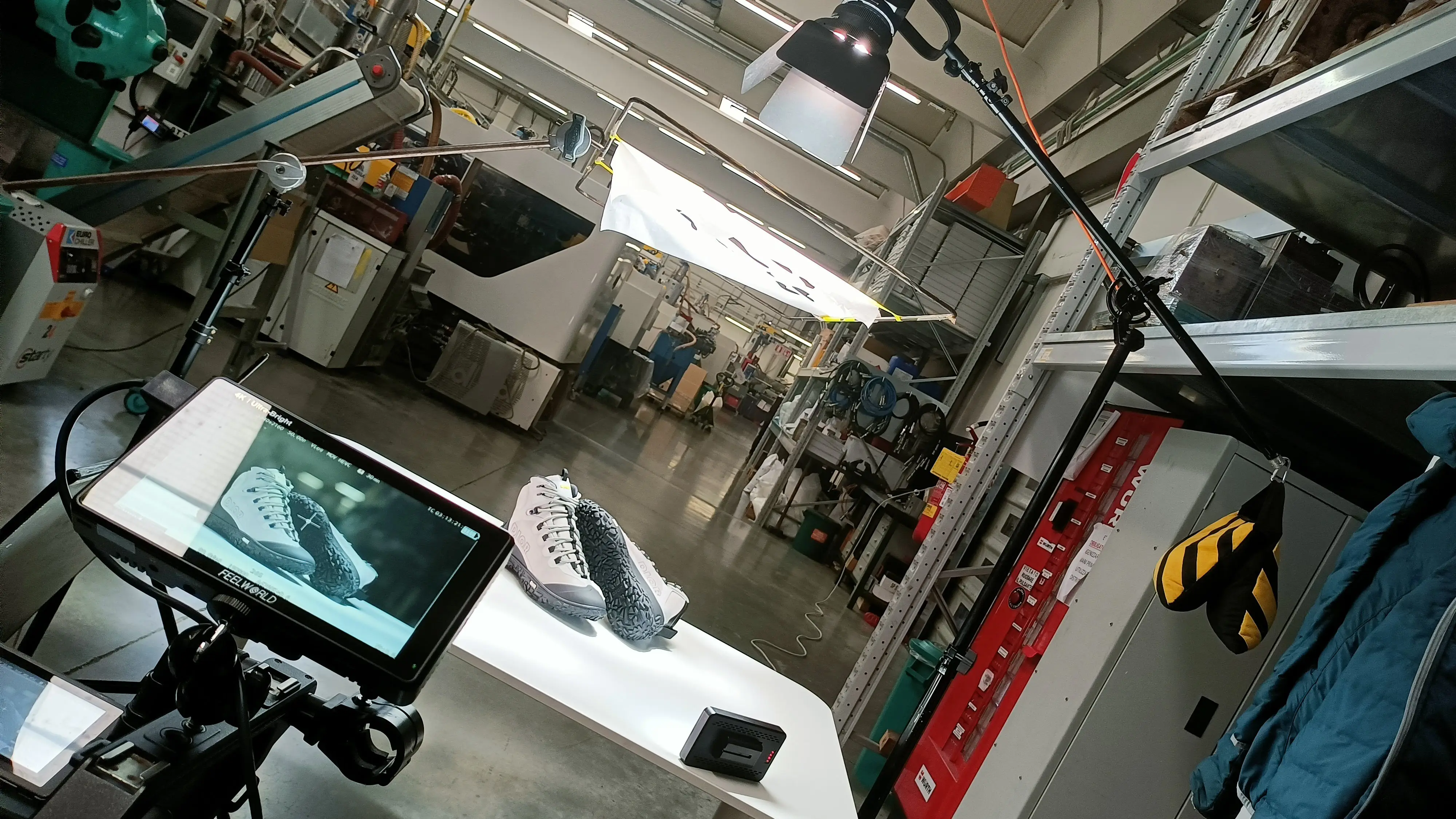 Wide view of a product set built inside a shoe factory, with camera, monitor and lights around a single sneaker