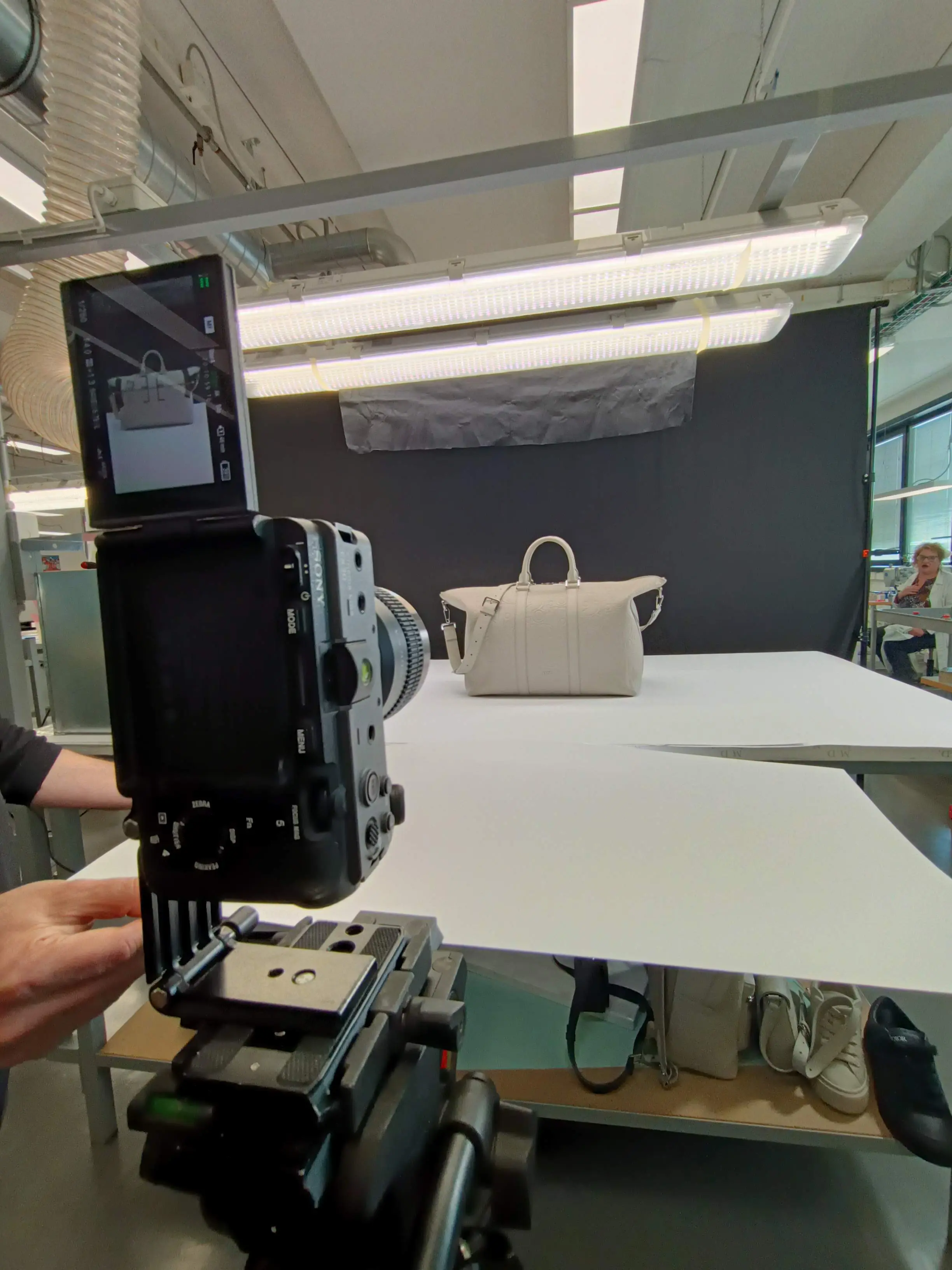 Handbag lit on a white table with a diffused overhead source, on a Dior product set
