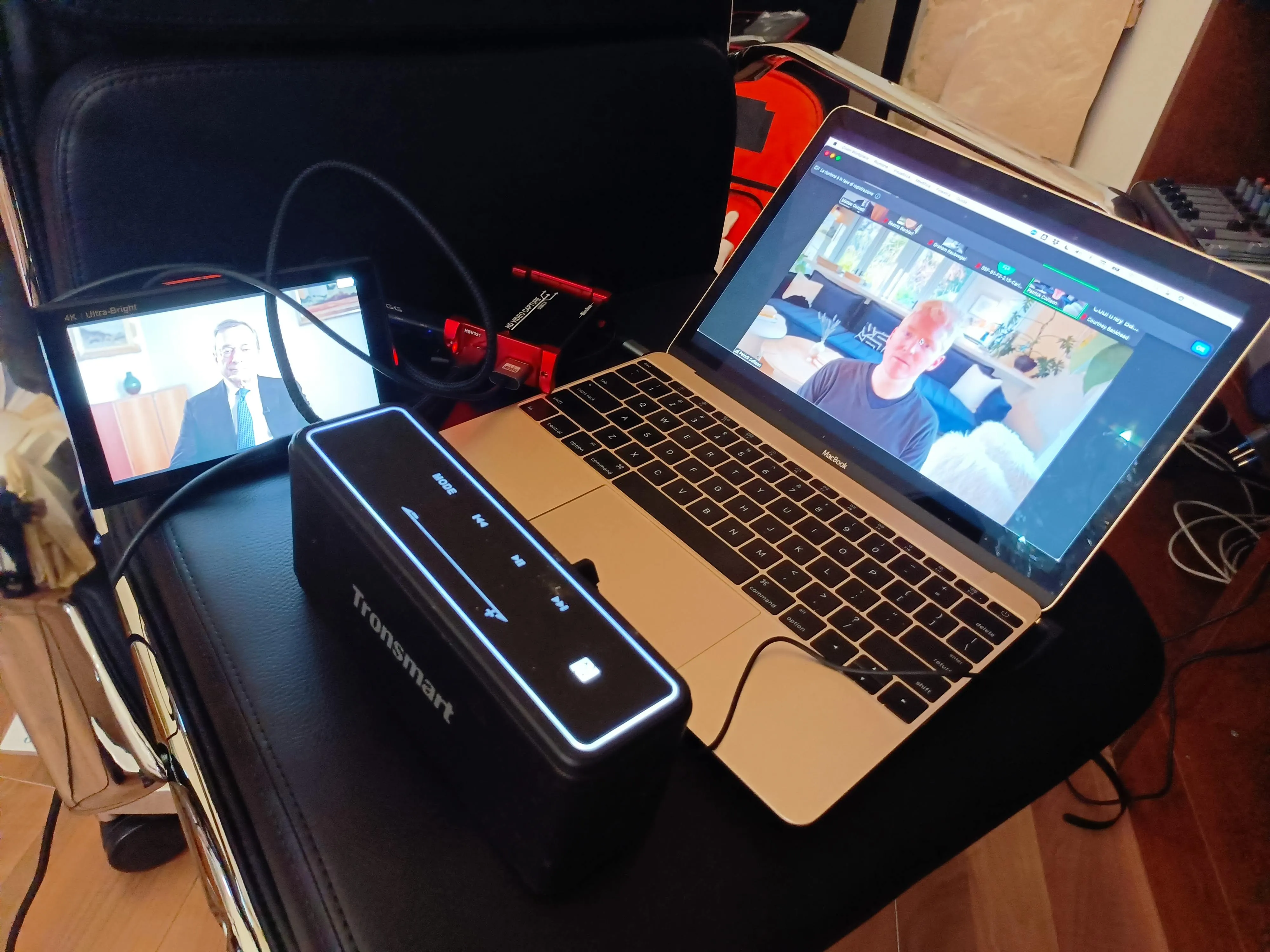 The remote link on a flight case: a field monitor showing Draghi, an HDMI capture dongle and a laptop carrying the video call with the interviewer in California