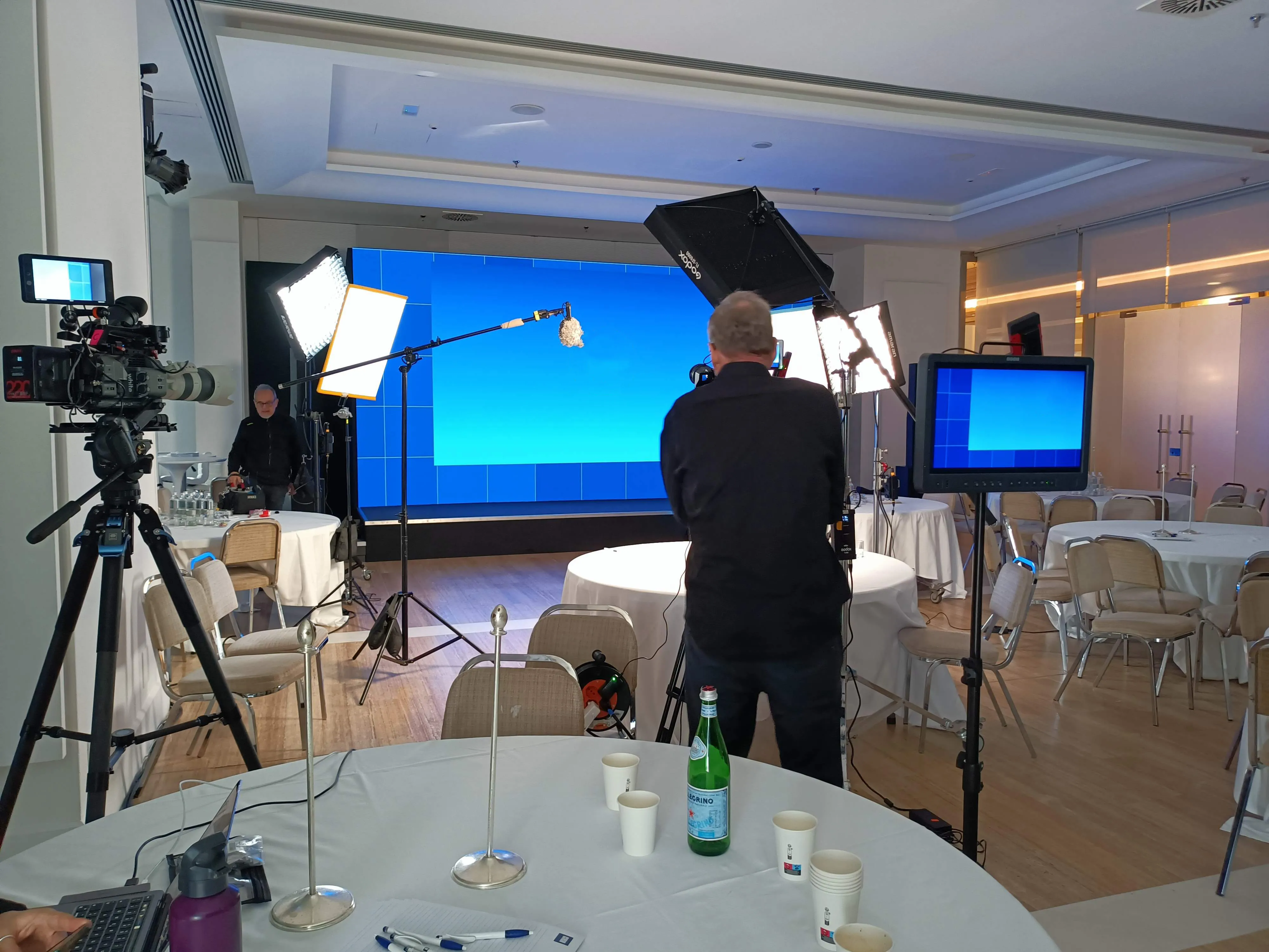 Interview position set up in the convention ballroom: a Sony camera on sticks, Aputure LED panels, a boom overhead and a client monitor beside the LED wall