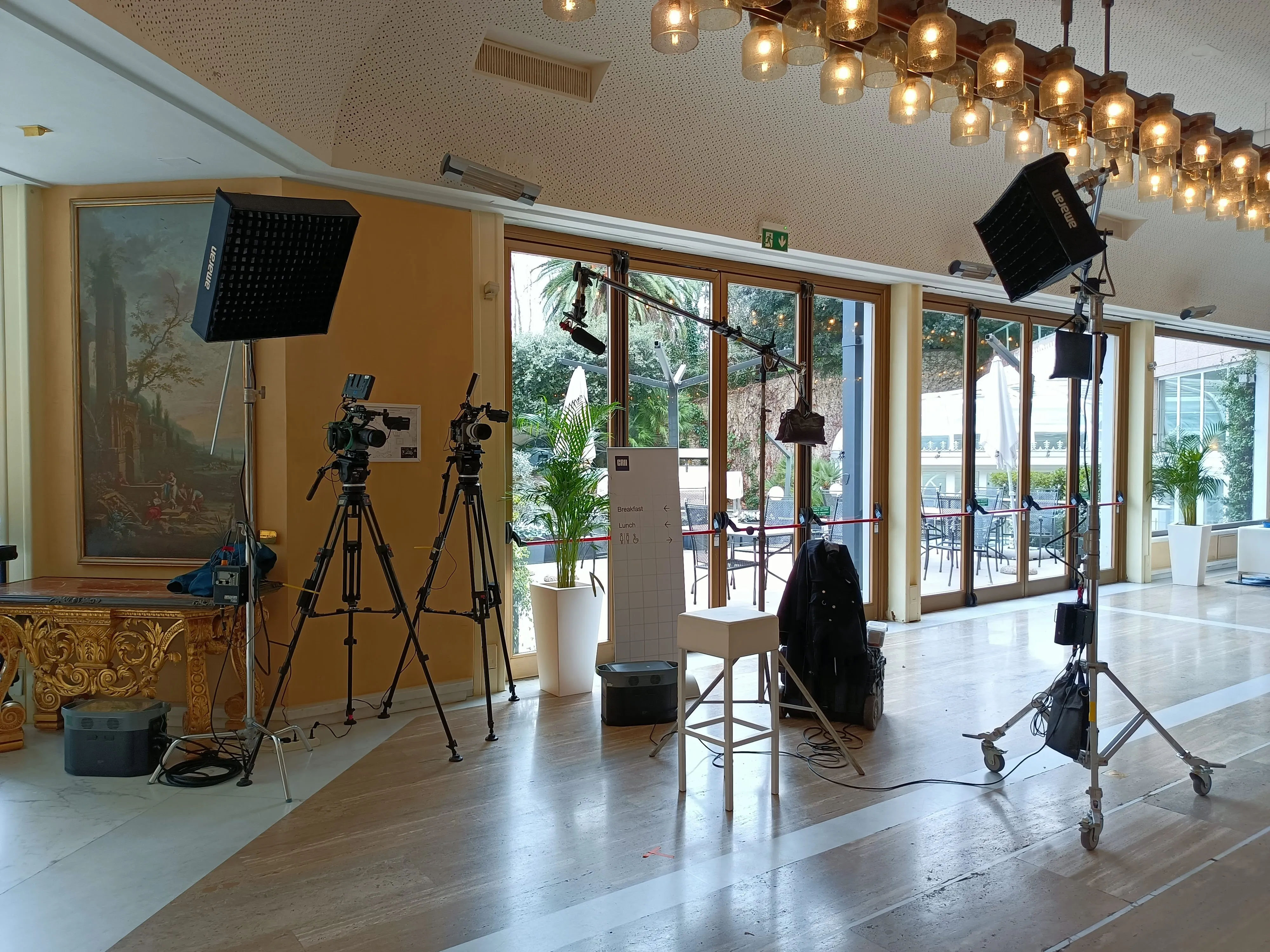 Two-camera corporate interview setup in a grand hotel lobby with boom microphone and Amaran LED panels