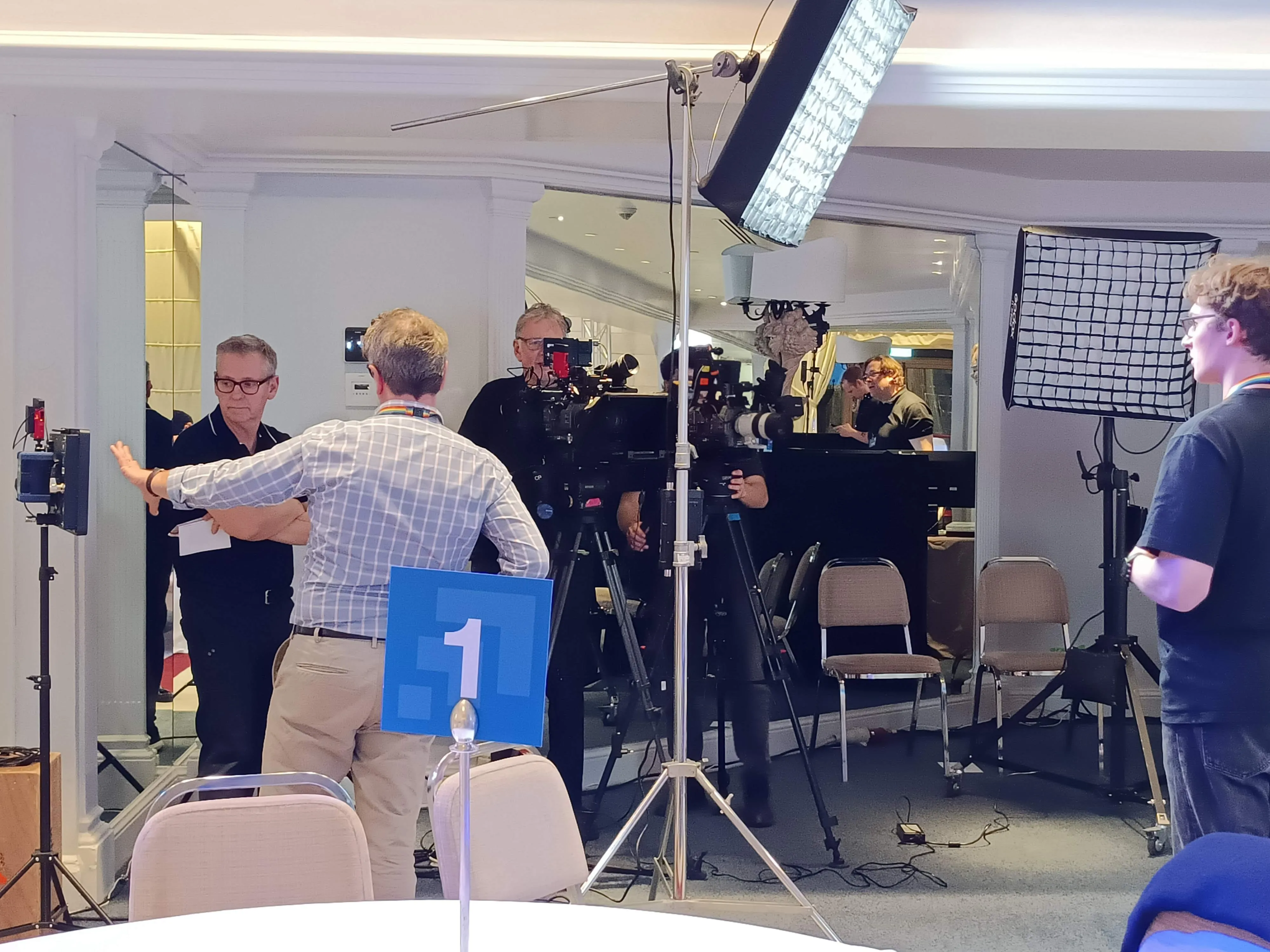The main unit in the hotel: two cameras side by side on tripods under an overhead softbox, with the crew setting the shot
