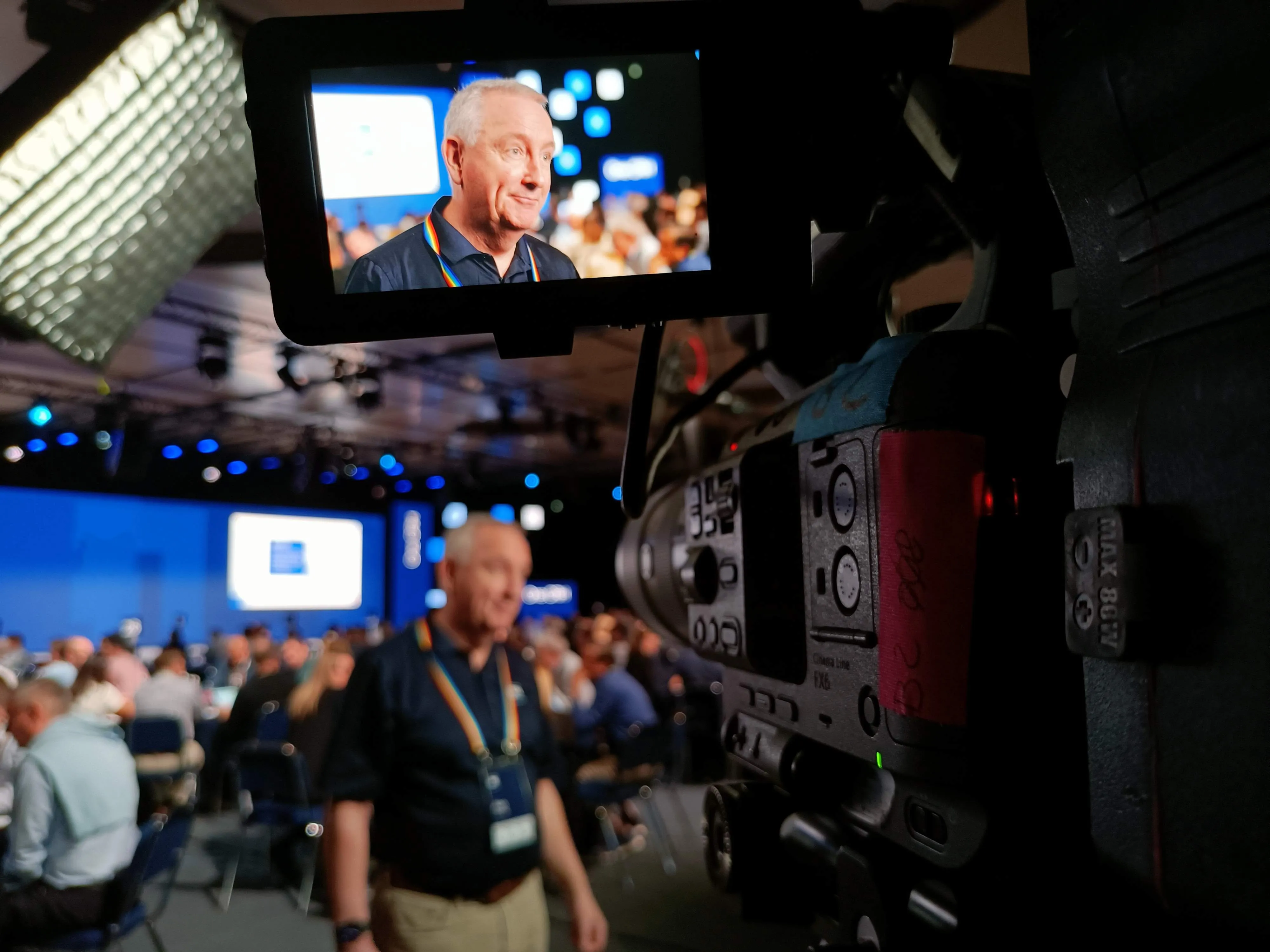 Roaming coverage in the plenary hall: the monitor of a Sony FX6 framing a delegate, with the audience and the stage screens behind