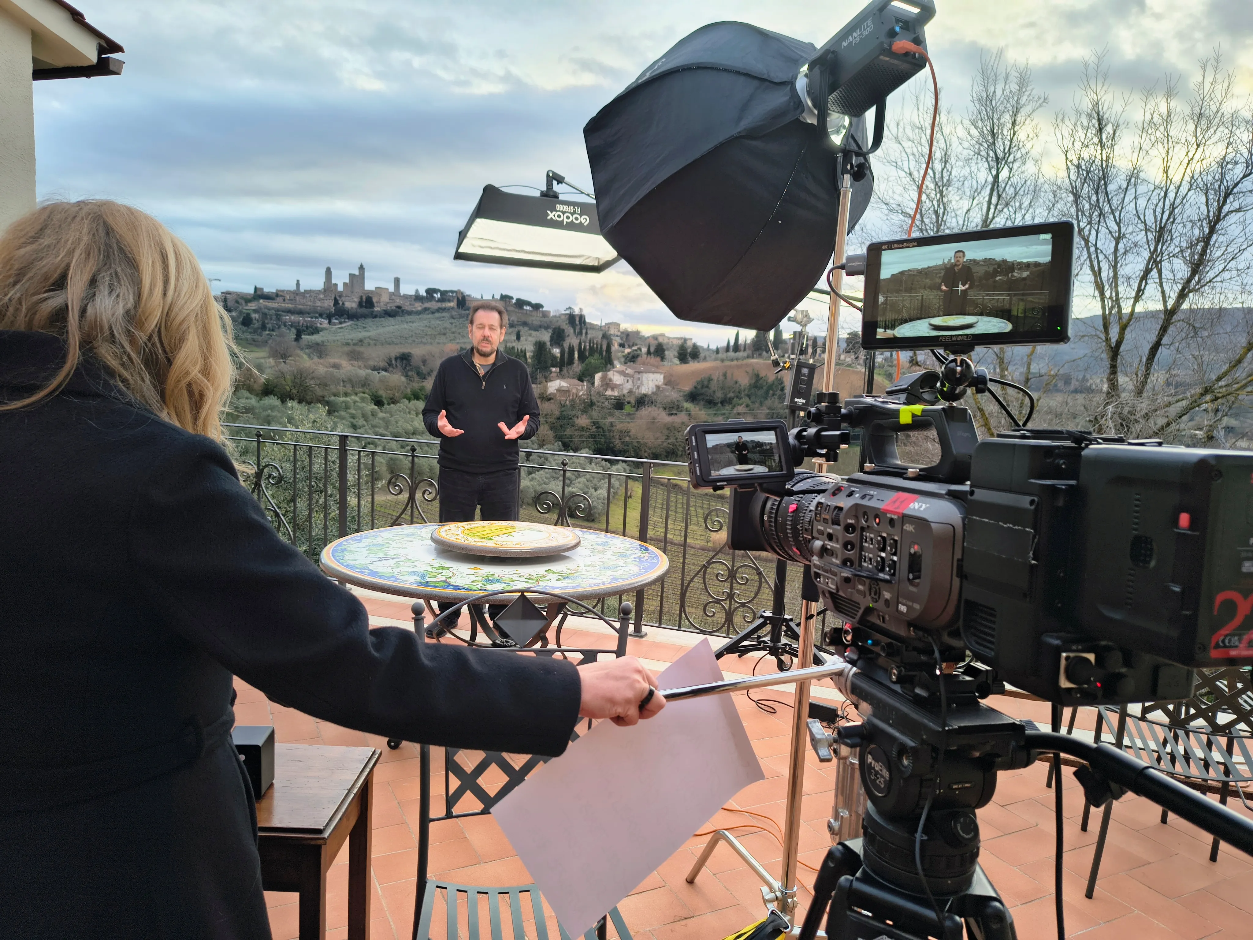 Rehearsal on the terrace the day before the broadcast: a Nanlite FS-300 through a softbox, a Godox flexible panel on a boom and a Sony FX9 with two monitors, with San Gimignano on the hill behind