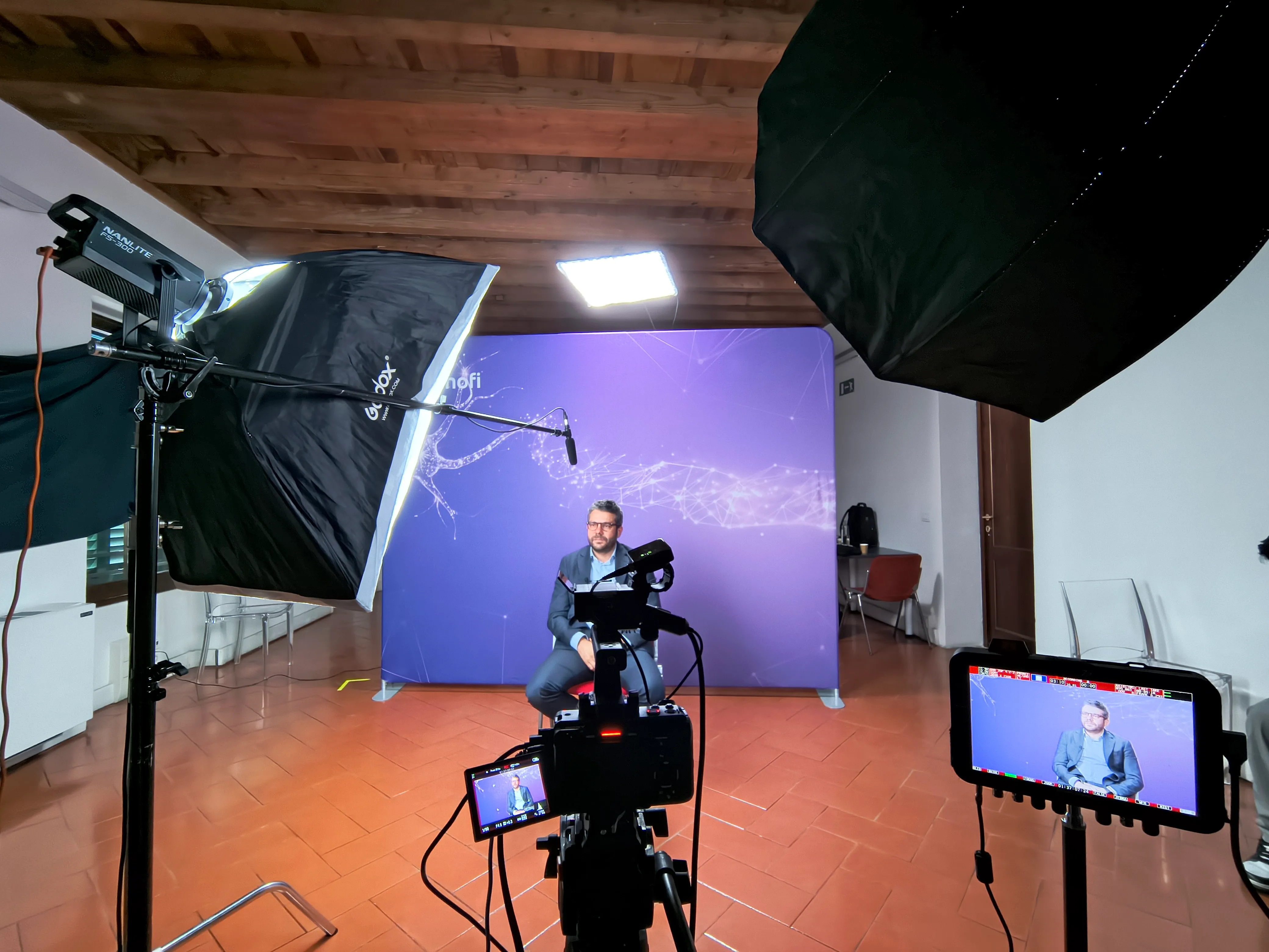 Corporate interview against a branded backdrop, filmed with two cameras, softboxes and a boom microphone