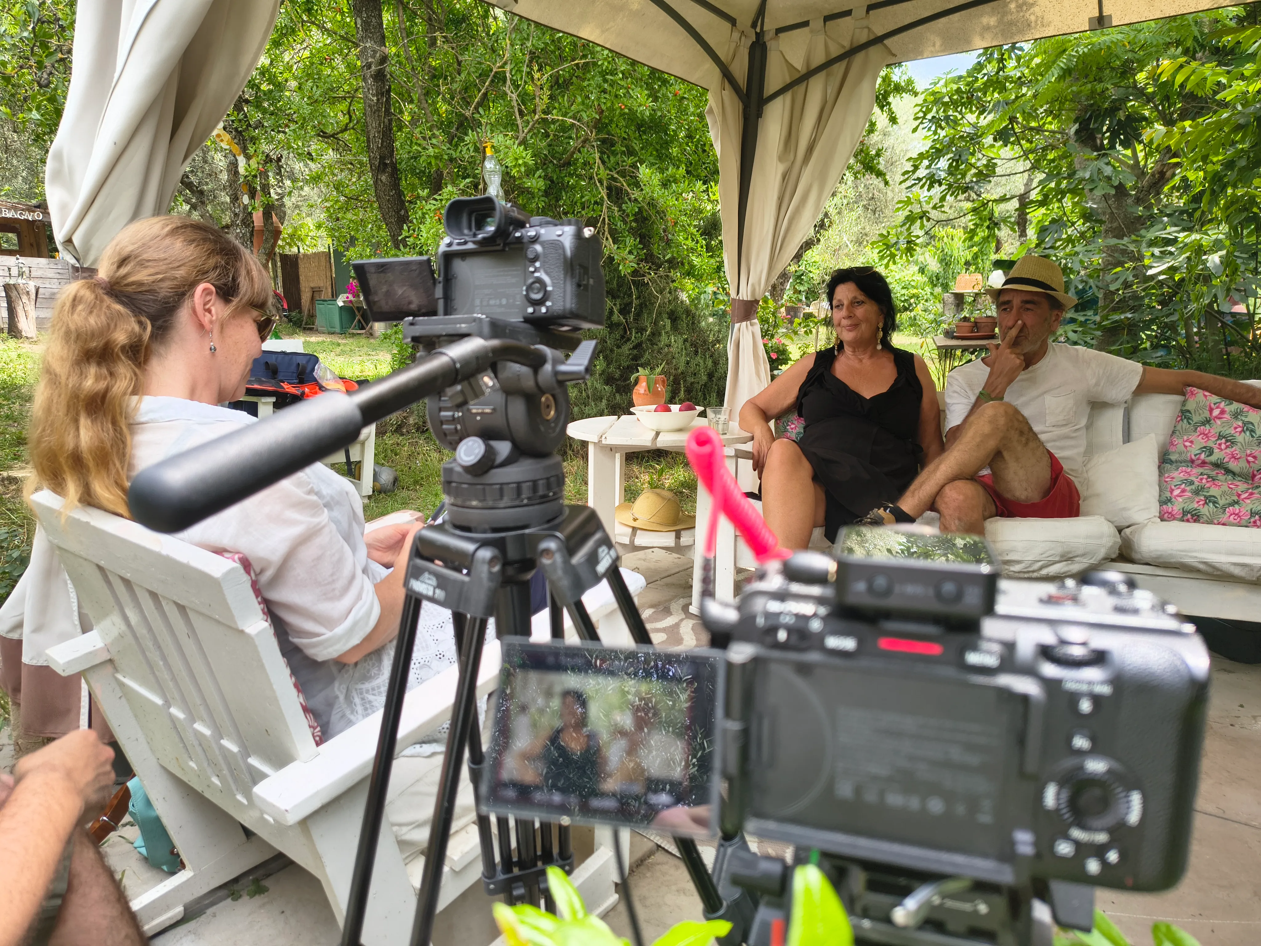 Two-camera interview with a couple under a garden gazebo, the interviewer seated off camera, for a Smart Move Italy documentary